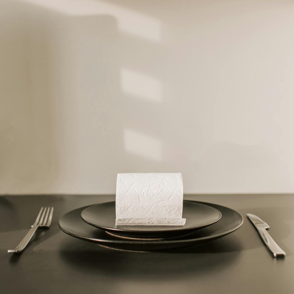 A humorous table setting with toilet paper as the main dish on elegant black plates.