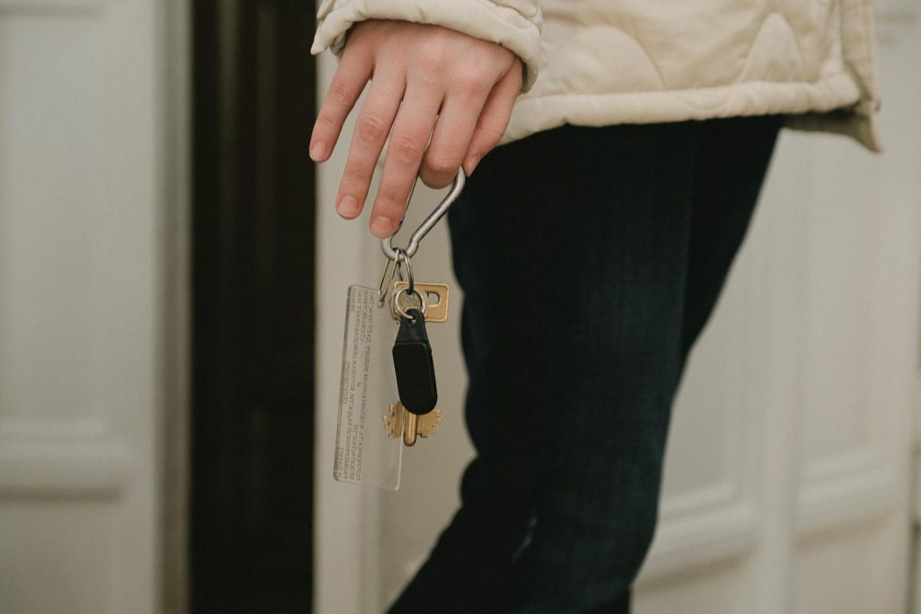 A close-up photo of an adult hand holding a set of house keys indoors, suggesting security and home access.